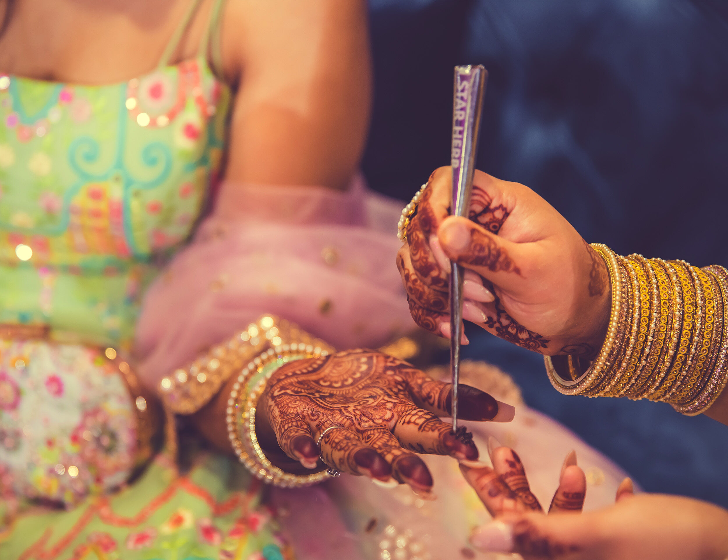 Bride sitting gracefully while a professional Mehendi artist applies an intricate henna design.